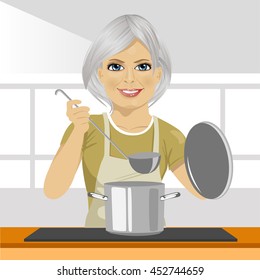 Smiling mature woman with ladle cooking soup in pan at domestic kitchen