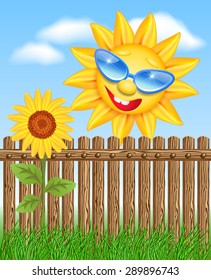 Smiling sun peeks out from behind a fence and looks at sunflowers