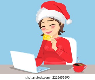 Smiling woman excited doing online Christmas shopping sitting wearing red Santa hat holding her golden credit card to use on her laptop computer. X-mas gift list concept.