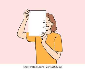 Smiling woman holding piece of paper with emoji in front of face and looking at screen. Positive girl with partially painted smile is sharing good mood and positive emotions with you.