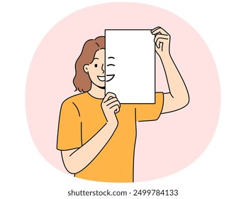 Smiling woman holding piece of paper with emoji in front of face and looking at screen. Positive girl with partially painted smile is sharing good mood and positive emotions with you.