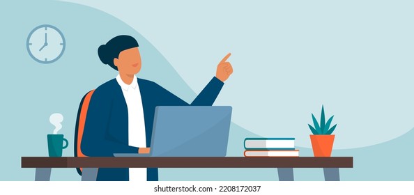 Smiling woman sitting at office desk, she is working with a laptop and pointing upwards, remote work and technology concept, blank copy space