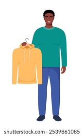 Smiling young black man holding hanger with yellow hoody. Choosing clothes concept. Vector illustration in flat style