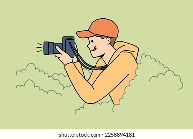 Lächelnder junger Mann versteckt sich in Büschen machen Bilder mit professioneller Kamera. Glücklicher Journalist oder Reporter fotografieren aus verstecktem Ort. Vektorgrafik. 