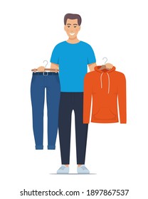 Joven sonriente sosteniendo perchas con pantalones y sudaderas. Elegir el concepto de ropa. Ilustración vectorial en estilo plano