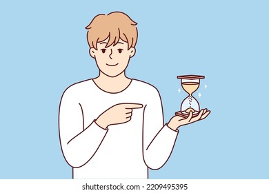 Smiling Young Man Point At Sandglass Show Sand Flowing And Time Passing. Happy Male Show With Finger And Hourglass. Vector Illustration. 