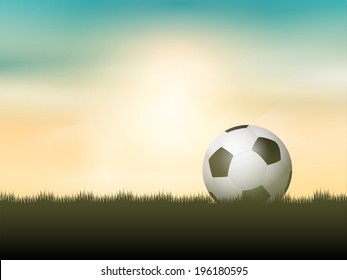 Soccer ball or football nestled in grass against a sunset sky