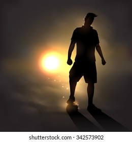 futbolista parado con un balón de fútbol al atardecer