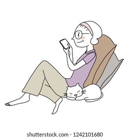 Social network concept with mature woman reclining on pillows comfortably with sleeping cat, reading text message and texting on her smartphone. Woman sitting, relaxing and reading message from phone.