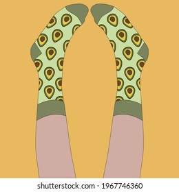 Socks with an avocado print are worn on the legs. The man lies with his legs up and looks at his socks. Green socks, orange background