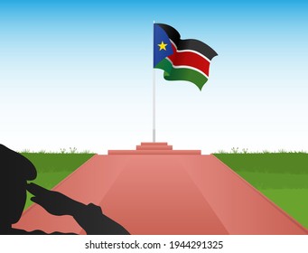The South Sudan flag flies above the pole in the shadow of a soldier saluting the flag