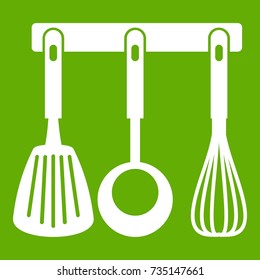 Spatula, ladle and whisk, kitchen tools on a hanger icon white isolated on green background. Vector illustration
