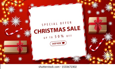 Special offer, Christmas sale, up to 50% off. Red discount banner with gifts, candys cane, paper snowflakes, garland and paper white sheet with offer on red table, top view