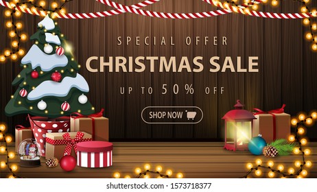Special offer, Christmas sale, up to 50% off, beautiful discount banner with Christmas decor, garlands, vintage lantern and Christmas tree in a pot with gifts near the wooden wall