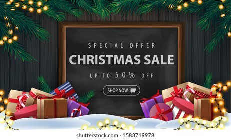 Special offer, Christmas sale, up to 50% off, discount banner with wooden wall, Christmas tree branches, garland, chalk board with offer and presents