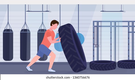 sports man flipping a tire doing hard exercises guy working out in gym with punching bags crossfit training healthy lifestyle concept modern health club interior horizontal