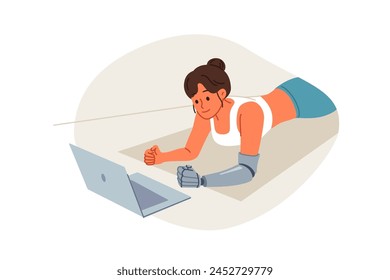 Sports woman with prosthetic arm trains at home and watches video lesson on laptop, lying on floor in plank. Sports girl doing yoga on fitness mat, training to improve health and muscle development