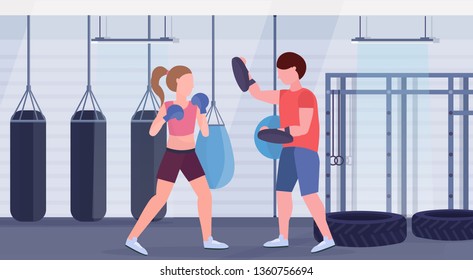 sportswoman boxer doing boxing exercises with personal trainer girl fighter in blue gloves working out fight club with punching bags gym interior healthy lifestyle concept