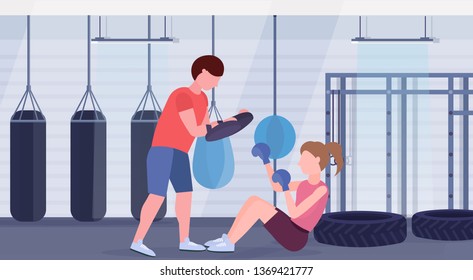 sportswoman boxer doing boxing exercises with personal trainer girl fighter in blue gloves working out on floor fight clubwith punching bags gym interior healthy lifestyle concept horizontal