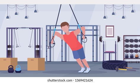 sporty man doing exercises with suspension fitness straps elastic rope guy training  workout concept modern gym studio interior horizontal flat full length