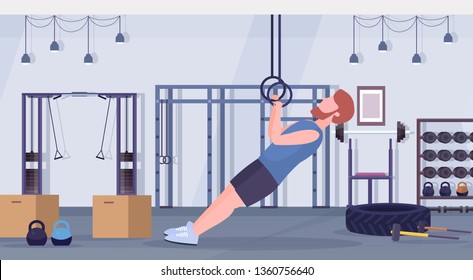 sporty man doing ring dips exercises with gymnastic rings guy training cardio crossfit workout concept modern gym health club studio interior horizontal full length