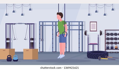 sporty man doing ring dips exercises with gymnastic rings guy training cardio  workout concept modern gym health club studio interior horizontal full length