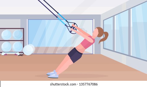 sporty woman doing exercises with suspension fitness straps elastic rope girl training crossfit workout concept modern gym studio interior horizontal flat full length