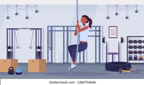 sporty woman doing rope climbing exercise african american girl training cardio crossfit workout concept modern gym health studio club interior horizontal flat full length