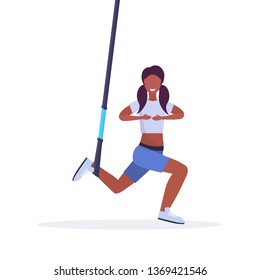 sporty woman doing squats exercises with suspension fitness straps elastic rope african american girl training in gym  cardio workout concept flat white background full length