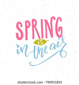 Spring is in the air. Inspirational quote about upcoming spring season. Pink and blue words and green leaf.