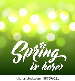 SPRING IS HERE Hand lettered style spring background. Handmade vector calligraphy on abstract glowing green background with bokeh light