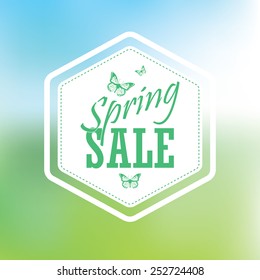 Spring sale poster with hexagonal badge. Typographic text, butterflies. Blurred background gradient mesh. Vibrant green for grass and blue for sky.