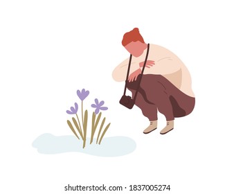 Squatting man admiring first spring flower or snowdrop. Teenager with camera sitting and looking at primrose. Flat vector cartoon illustration isolated on white background