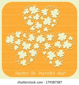  St. Patrick day card, many small paper clovers forming one big three leaf clover on orange background with wooden texture