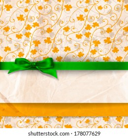 St. Patrick day card, silk green bow, white paper card decorated on patterned background with clovers and old crumpled paper texture
