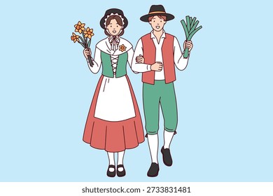 St Saint David's Day Eine lächelnde Frau in großen walisischen Hut hält einen Strauß von Narzissen, während neben einem Mann mit großen grünen Lauch beide in traditionellen Volkstrachten für eine nationale Veranstaltung gekleidet stehen