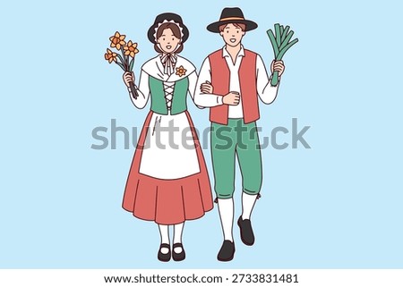 St Saint David's Day A smiling woman in tall Welsh hat holds a bouquet of daffodils while standing next to a man holding large green leek both dressed in traditional folk costumes for a national event