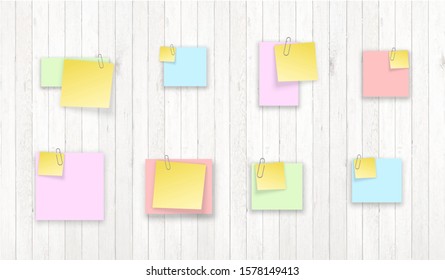 Stack of colored stickers attached metal paper clip with curled corner, ready for your message. Set of color stickers isolated on white wooden boards wall background. illustration set paper Front view