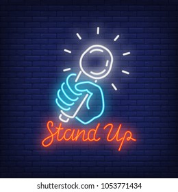 Stand up neon sign. Microphone in human hand on brick wall background. Night bright advertisement. Vector illustration in neon style for comedy show