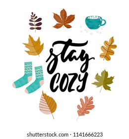 Stay cozy - hand drawn Autumn seasons holiday lettering phrase and Hugge doodles with leaves, cup of tea, cocoa, chocolate, warm socks isolated on white. Ink illustration for banners, cards, posters