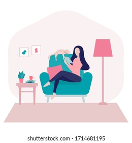 Stay home concept. Young woman sitting on armchair at home with her cat and surfing on the internet using a tablet in a period of self-isolation and social distancing.