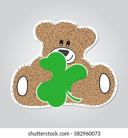 Sticker cartoon illustration - sitting and smiling brown, furry bear with green clover in the hands. White outline with shadow.