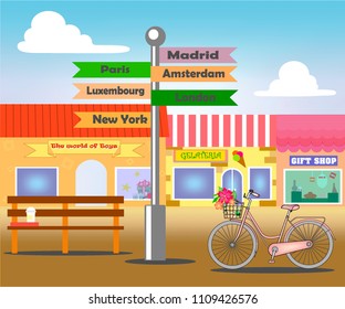 Street with shops, on the street there is an index with famous capitals, a shop and a women's bicycle