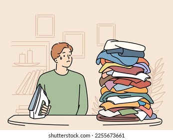 Joven estresado mira la pila de ropa para planchar. Un tipo infeliz que estaba angustiado con pilas de ropa para planchar. Tareas domésticas. Ilustración vectorial. 