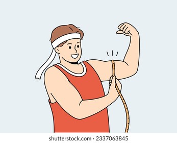 Strong man shows biceps and uses measuring tape to check size of muscles on arm. Strong guy in sportswear boasts about size of biceps and recommends doing bodybuilding or arm wrestling