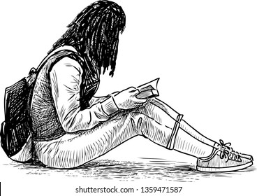 A student girl reads a book on the lawn in a city park