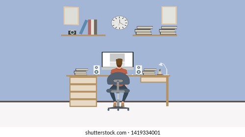 Student sitting behind his desk in studying room he is using his computer - back view