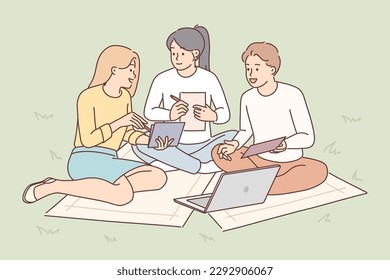 Students are sitting on lawn with laptop preparing joint extracurricular activity assigned by college or university teacher. Guy and girls are working in park making collaboration for brainstorming 