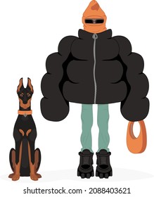 Stylish guy in a big black winter coat, orange balaclava, blue jeans, bulky boots and orange bag poses with a Doberman
