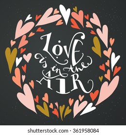 Stylish romantic invitation card template or wedding element with frame made of colorful doodle hearts on chalkboard background. 'Love is in the air' hand lettering inspirational quote.